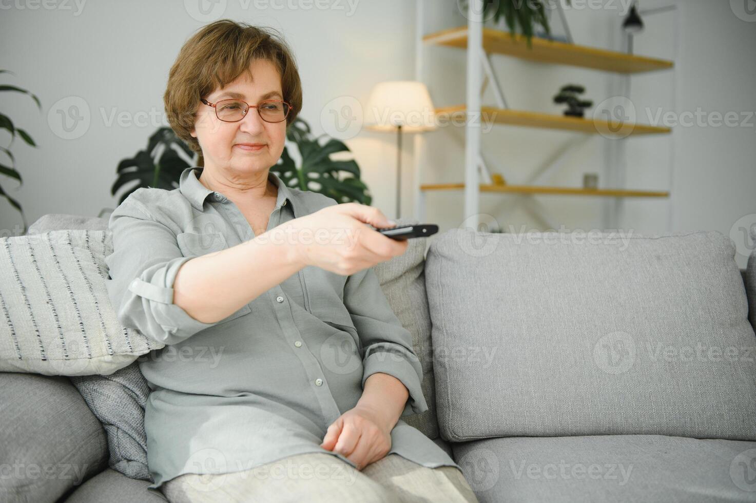 rupture nouvelles. sous le choc Sénior femme en train de regarder la télé à maison, séance sur canapé avec éloigné manette dans mains photo