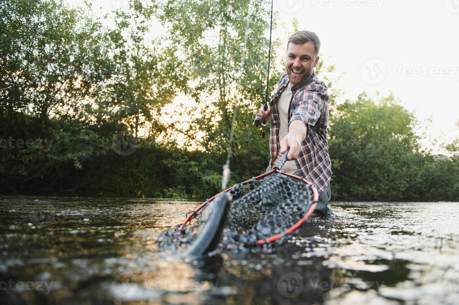 homme avec pêche canne à pêche, pêcheur Hommes dans rivière l'eau Extérieur. contagieux truite poisson dans filet. été pêche loisir photo