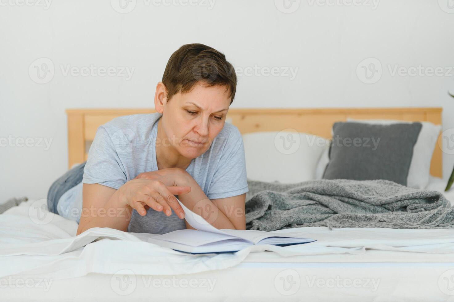 milieu âge blond femme en train de lire livre mensonge sur le lit à maison. photo