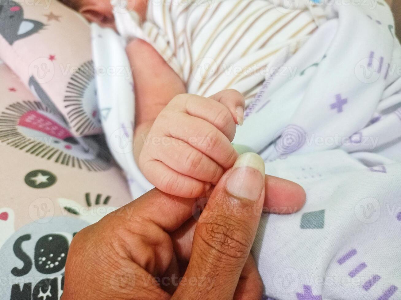 une père en portant le main de une nouveau née bébé tandis que il dort. photo