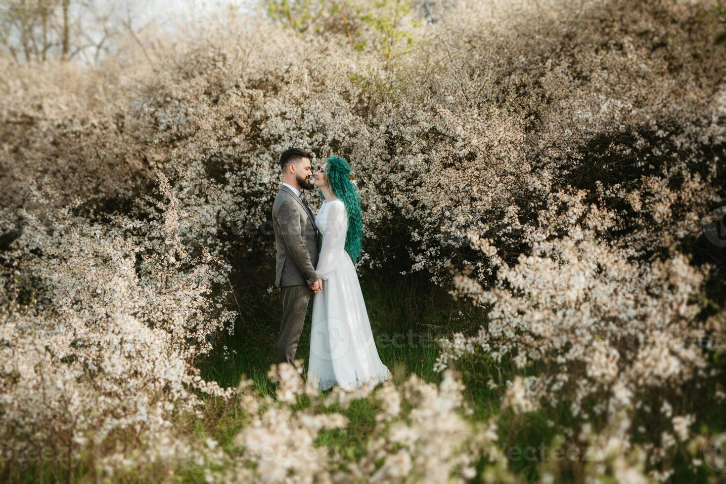 une barbu jeune marié pièces et une fille avec vert cheveux contre le Contexte de épanouissement printemps photo