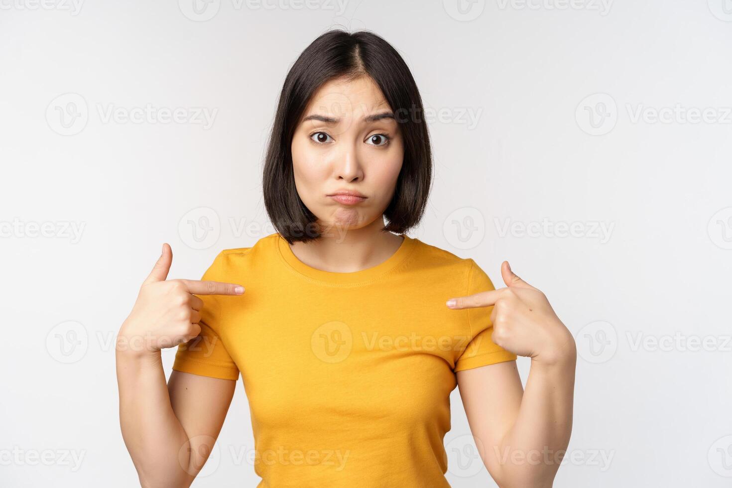 confus asiatique femme montrer du doigt à se, à la recherche dans incrédulité, permanent plus de blanc Contexte photo