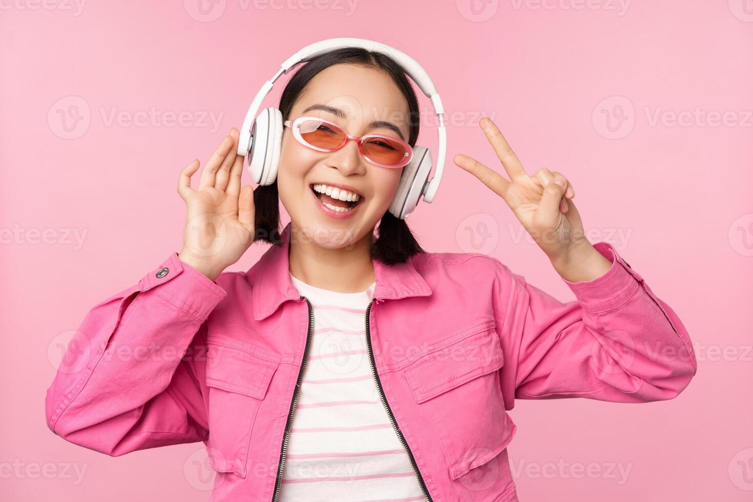 dansant élégant asiatique fille écoute la musique dans écouteurs, posant contre rose Contexte photo