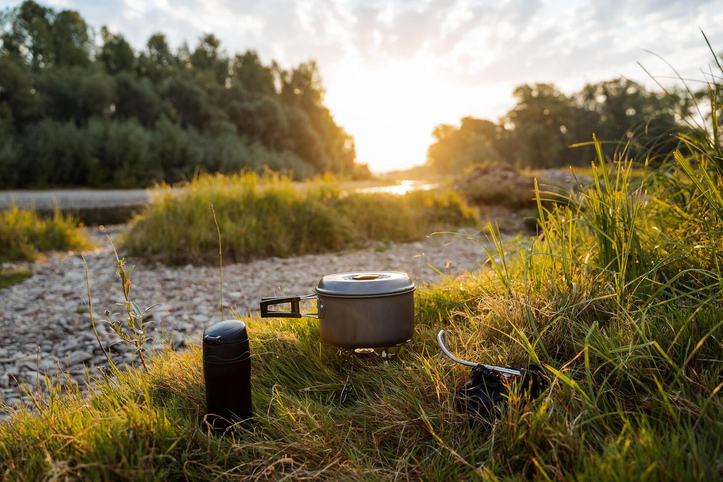 coucher de soleil, Aube sur une rocheux banque par le rivière avec une camping pot et une thermos, une horizontal Cadre. repas sur une randonnée, touristique aliments. Extérieur activités, été randonnées. photo