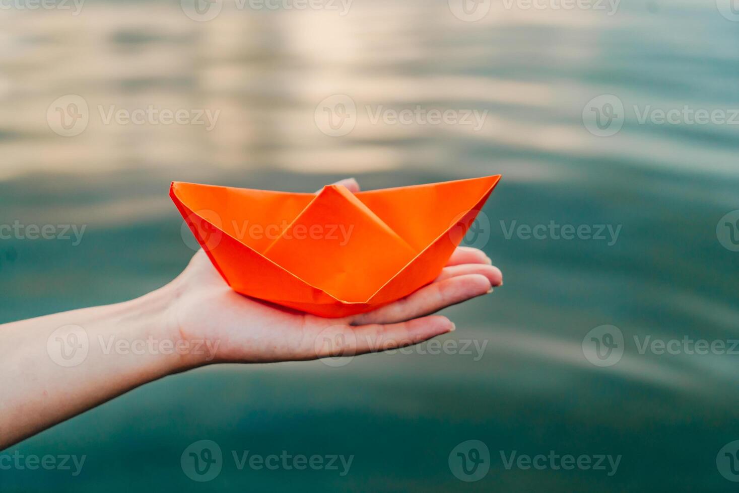 un Orange papier navire dans une femelle main plus de le l'eau. femme main en portant papier bateau au dessus le l'eau. fermer photo