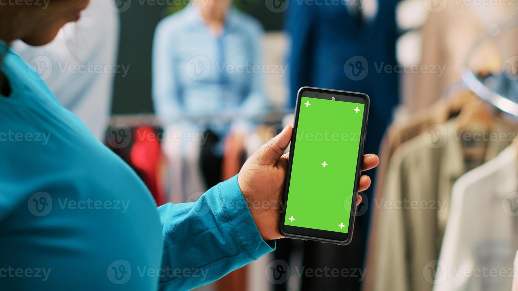 africain américain client en portant téléphone intelligent avec vert écran modèle, vérification mode boutique application. Shopaholic femme achat à la mode vêtements et branché accessoires dans achats centre photo