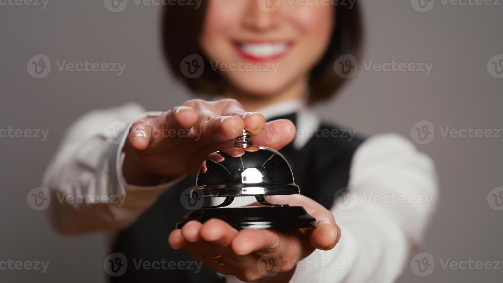 réceptionniste posant avec un service cloche et sonnerie il sur caméra, exprimer assistance de de face bureau personnel. asiatique Hôtel la conciergerie avec hospitalité industrie opérateur profession. proche en haut. caméra b. photo