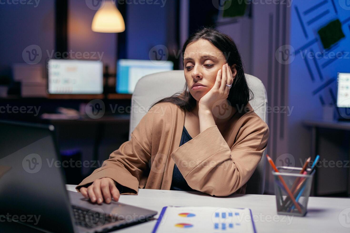 épuisé femme d'affaires à la recherche à ordinateur travail à terminer une date limite. intelligent femme séance à sa lieu de travail dans le cours de en retard nuit heures Faire sa emploi. photo