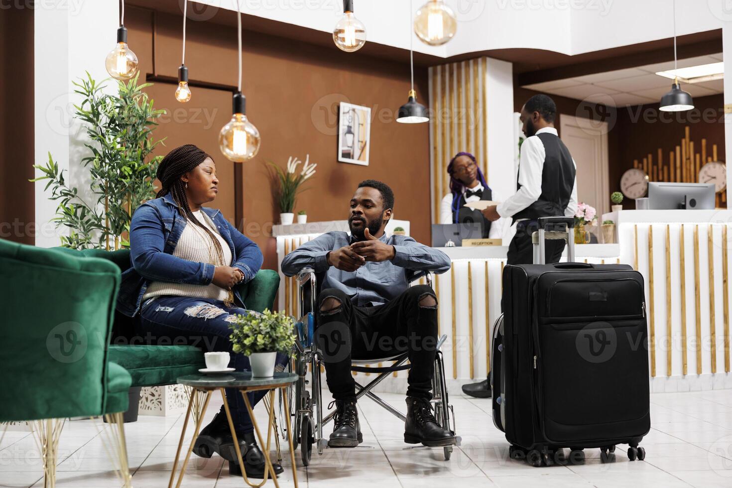 en voyageant avec fauteuil roulant utilisateur. fatigué malheureux couple femme et désactivée homme attendre pour enregistrement à station balnéaire, séance avec bagage dans Hôtel lobby, client un service pour invités avec handicapées photo