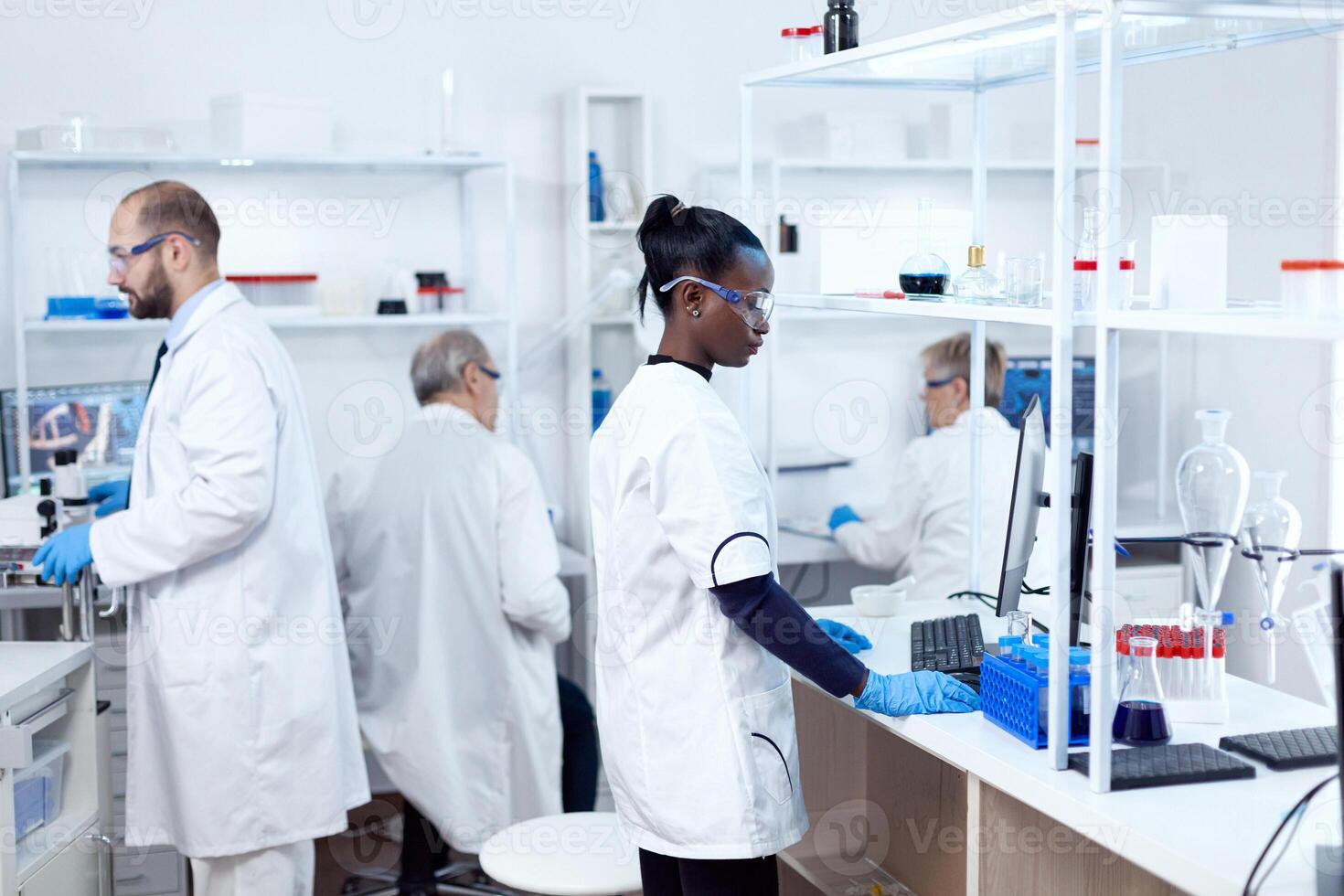 africain scientifique et sa collègues Faire expériences dans stérile laboratoire. Multi-éthnique équipe de des chercheurs travail dans microbiologie laboratoire essai Solution pour médical but. photo