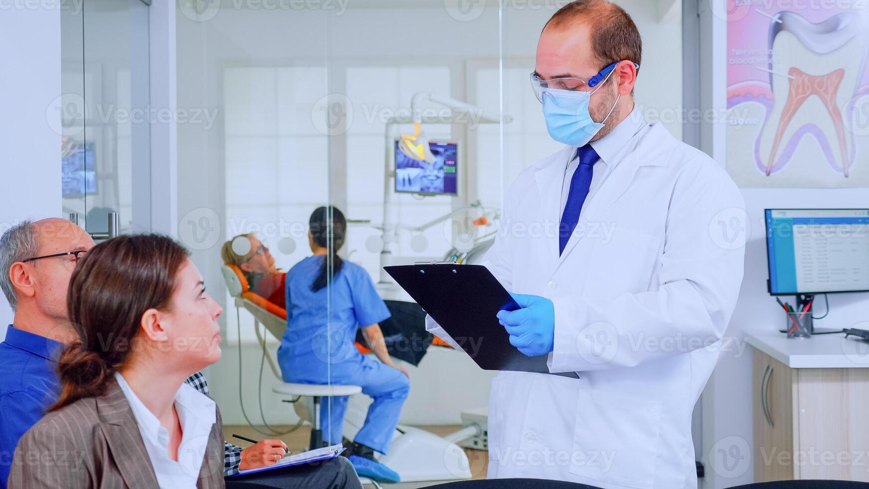 médecin prise Remarques sur presse-papiers à propos patient dentaire problèmes séance sur chaise dans attendre pièce de stomatologique clinique. assistant en train de préparer vieux femme pour examen dans Contexte photo