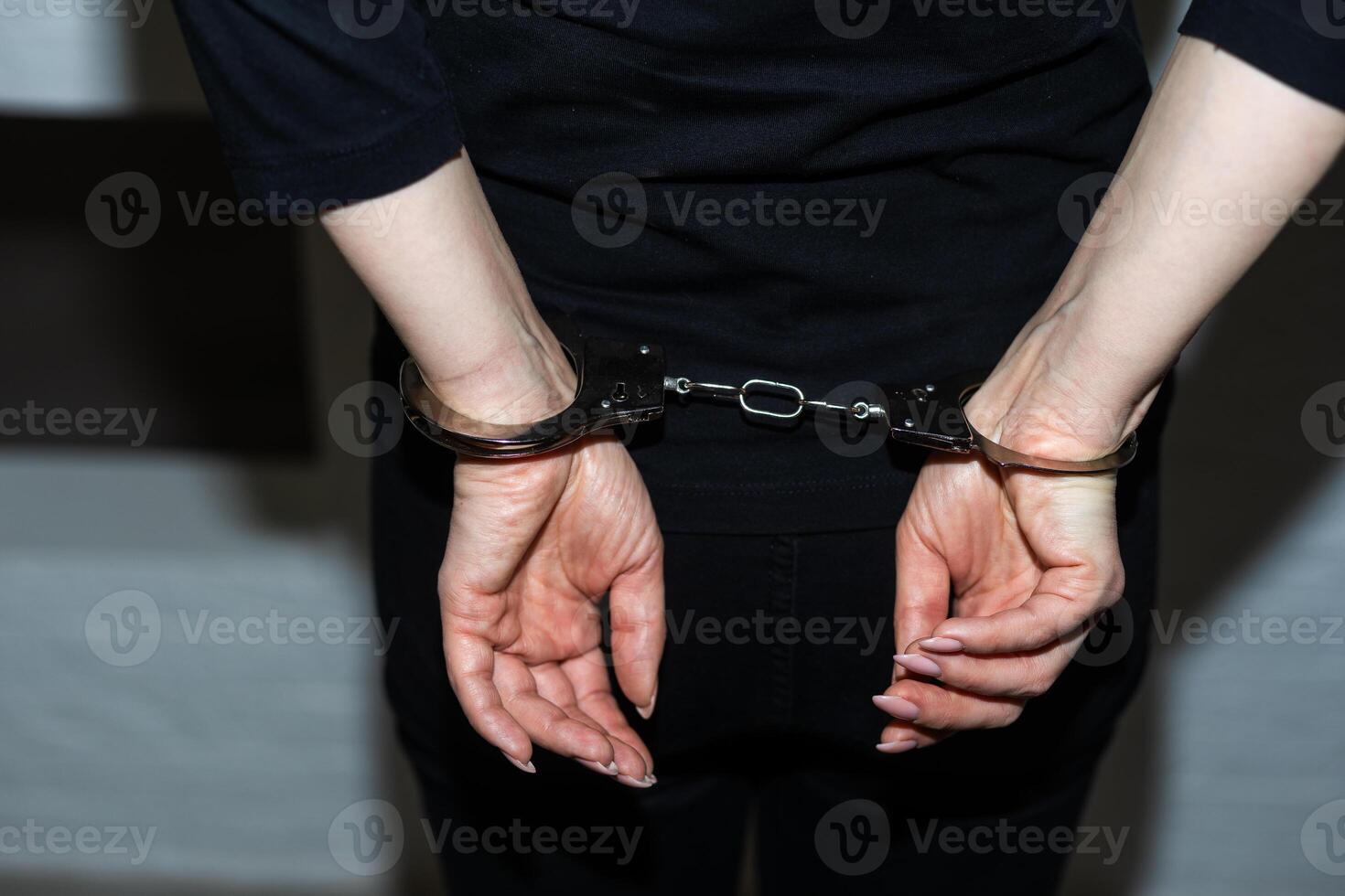 une femme qui a été arrêté et a sa mains menotté derrière sa retour à le arrière. le prisonnier est en attente transport à le prison. photo