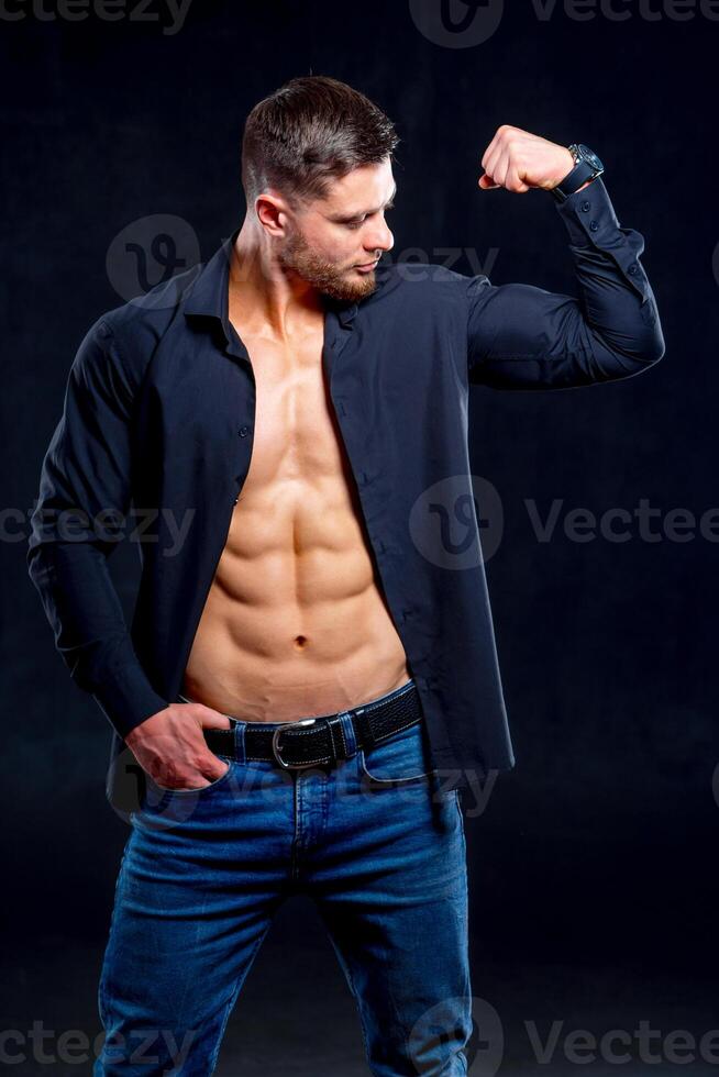 super sexy homme avec bronzer abdos et poitrine. athlétique homme avec déboutonné foncé chemise sur gris Contexte pompage muscles. studio portrait photo