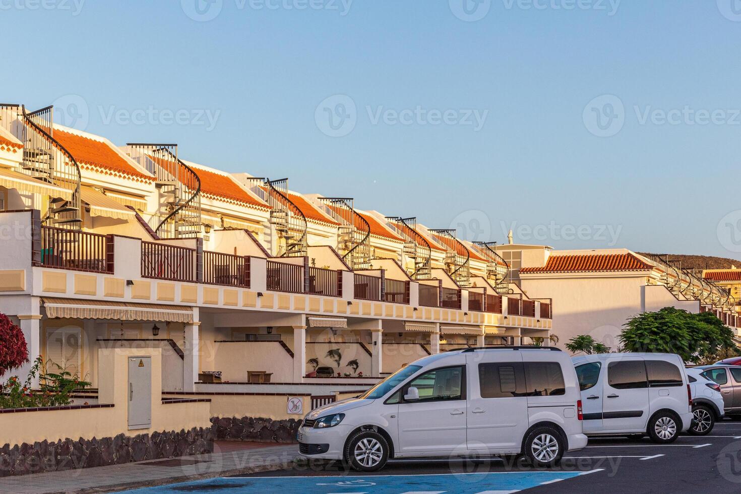 rangée de moderne maisons de ville avec balcons dans une Résidentiel zone, garé voitures dans devant, clair bleu ciel à crépuscule dans los chrétiens, tenerife. photo