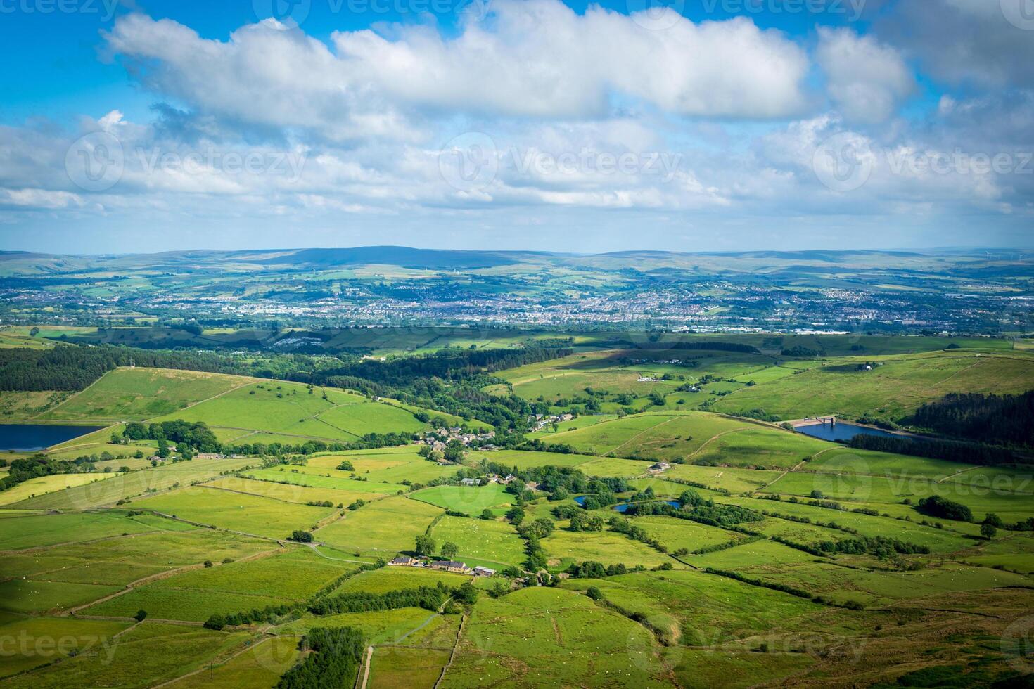 Stupéfiant aérien vue de luxuriant vert campagne avec roulant collines et patchwork les terres agricoles en dessous de une nuageux ciel. photo