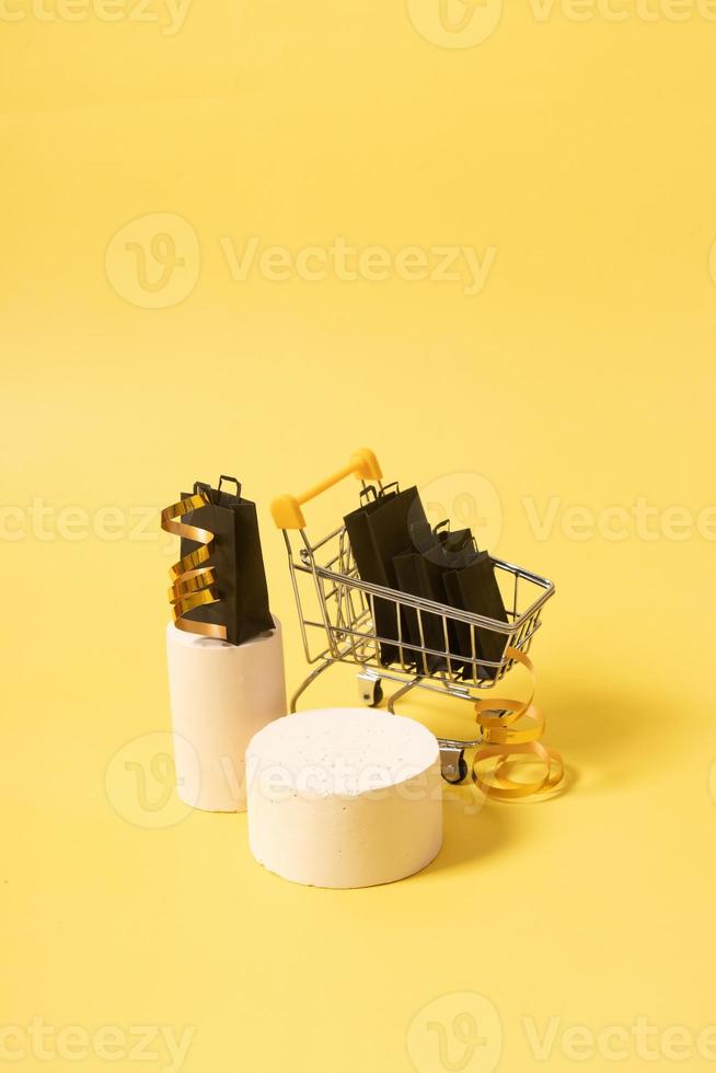 podium ou piédestal vide et chariot de supermarché miniature avec des sacs à provisions en vente vendredi noir sur jaune photo