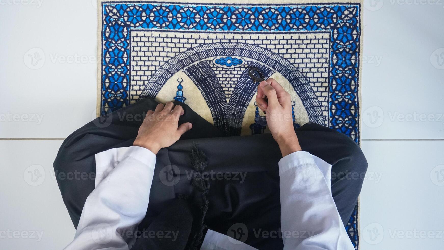 vue de dessus de l'homme musulman avec la main en prière sur le tapis de prière tout en tenant le chapelet photo