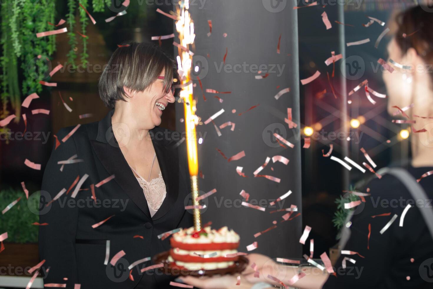 une âge moyen femme fête sa anniversaire. une femme se réjouit, regards à une anniversaire gâteau avec une brûlant bougie. photo