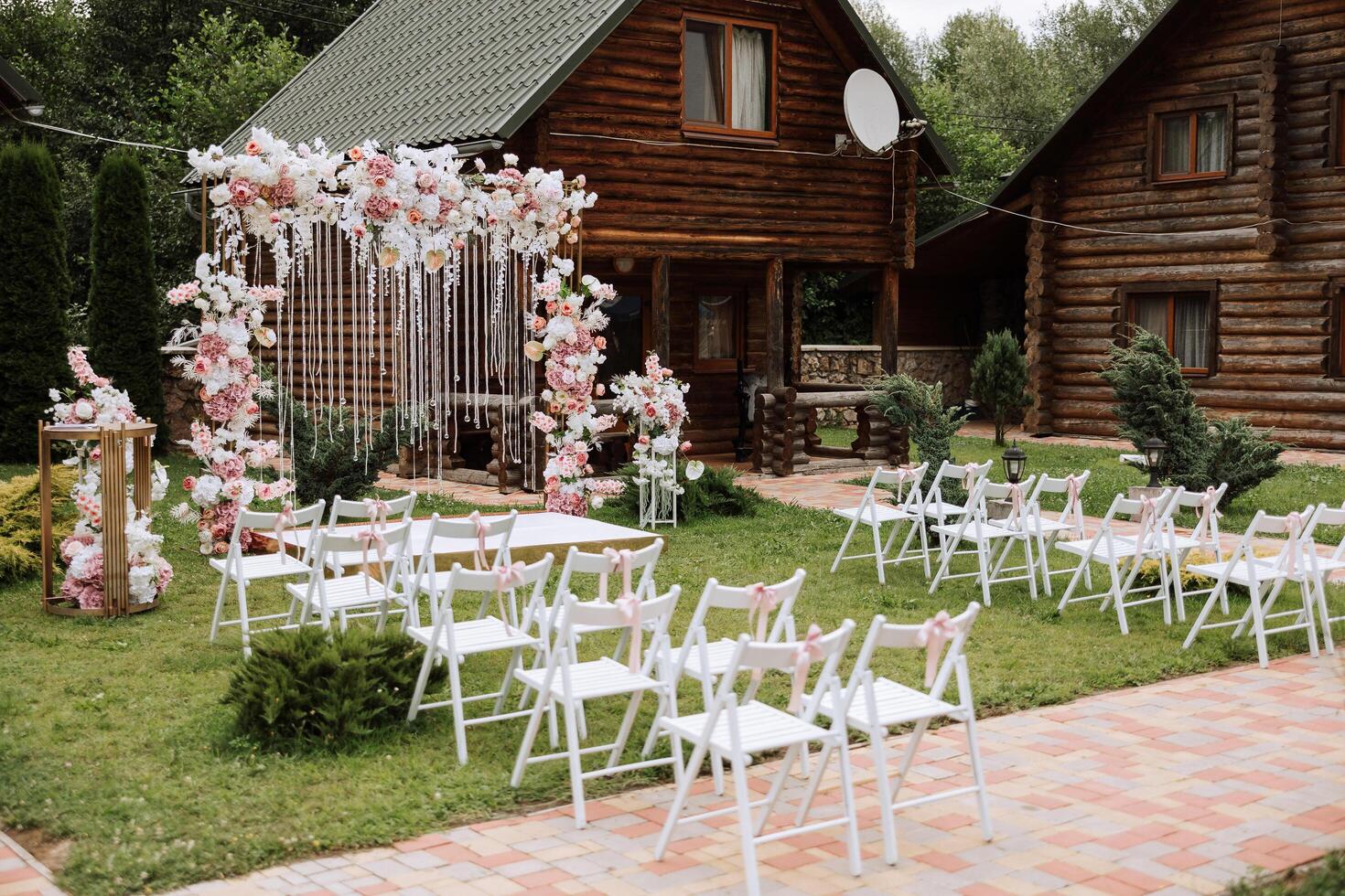 d'or cambre décoré avec fleurs sur le Contexte de des arbres. une blanc chemin cette pistes à le cambre, beaucoup blanc chaises. préparation pour le mariage la cérémonie photo