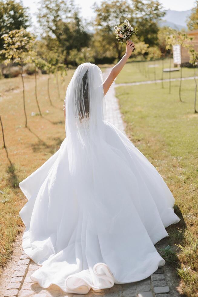 photo de le dos. une magnifique Jeune femme dans une blanc mariage robe est souriant sur une chaud mariage été journée