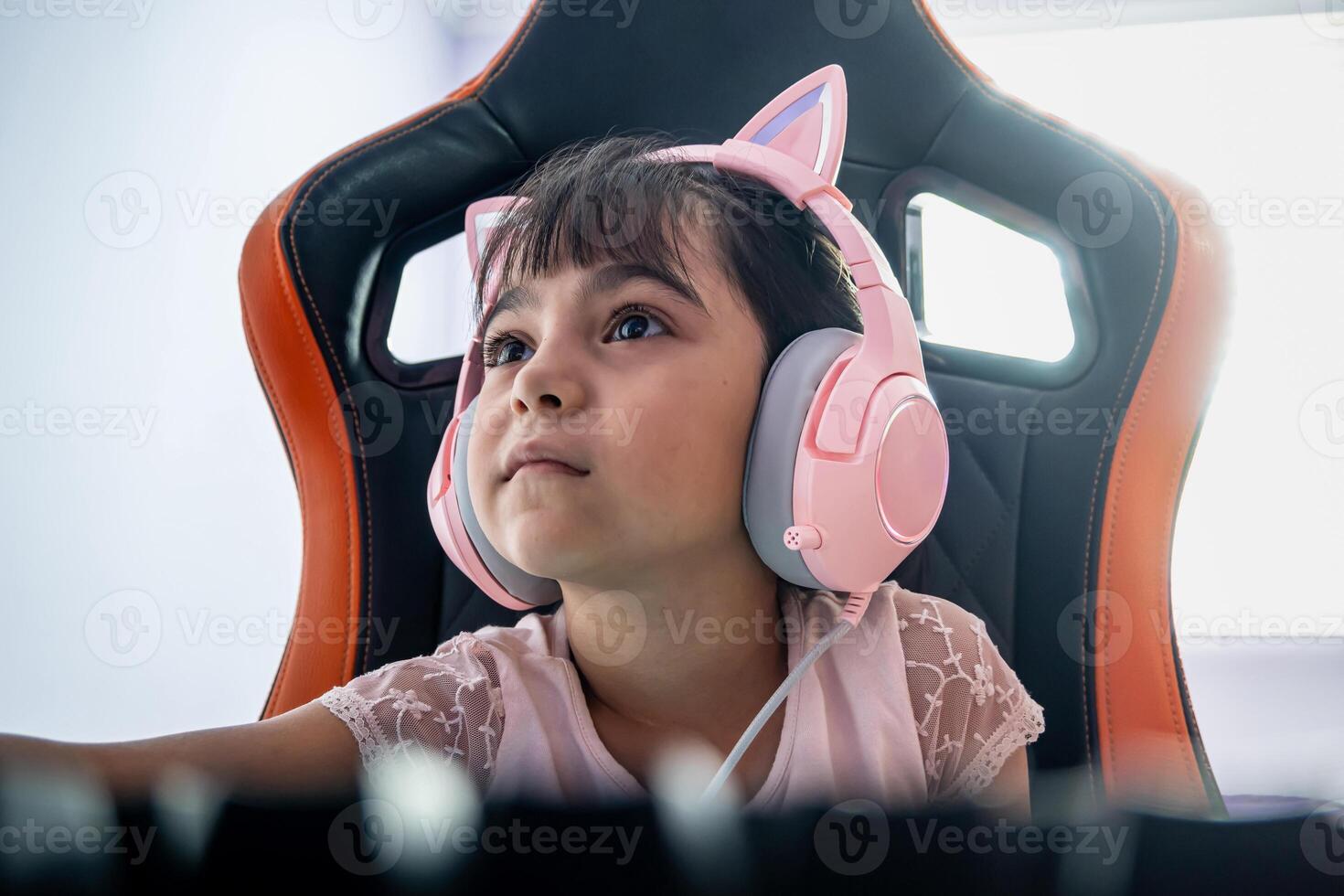 adorable joueur fille en jouant sur le ordinateur dans le chambre à coucher. elle est une peu fille portant magnifique écouteurs avec chat oreilles. photo