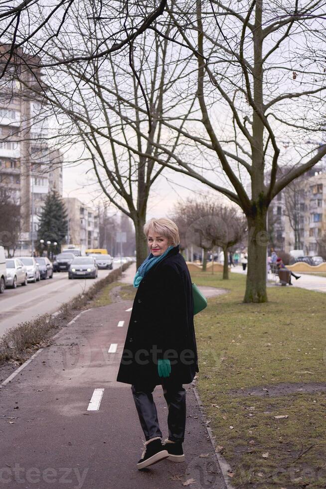 portrait de une élégant vieux femme dans une noir manteau avec vert accessoires sur une printemps rue photo