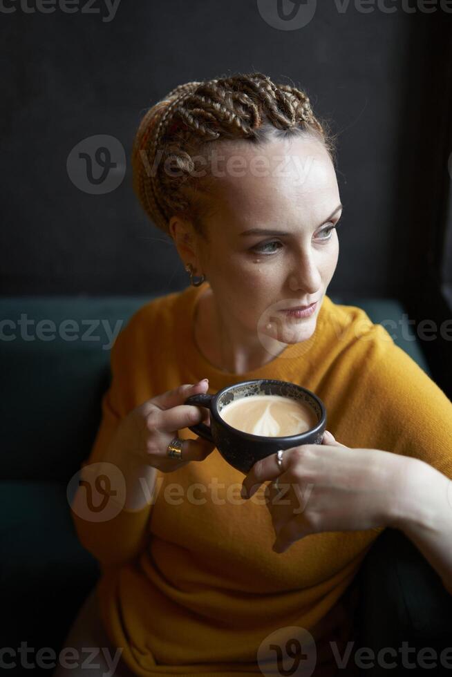 portrait de une élégant âge moyen femme dans une Jaune chandail en buvant café dans une café photo