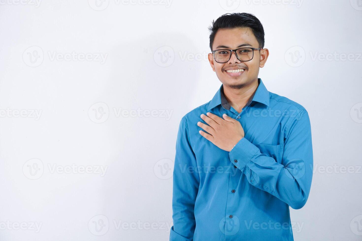 positif ou souriant asiatique employé homme en mettant mains sur le poitrine ou le respect personnage portant bleu chemise isolé sur blanc Contexte photo