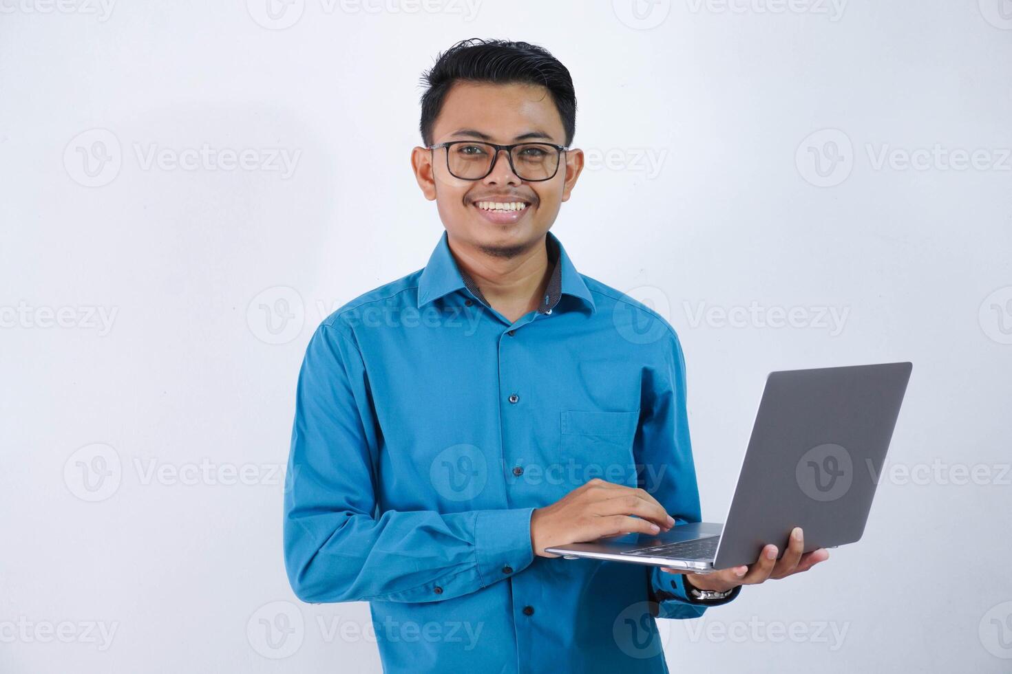 souriant ou content asiatique homme d'affaire avec des lunettes en portant portable portant bleu chemise isolé sur blanc Contexte photo