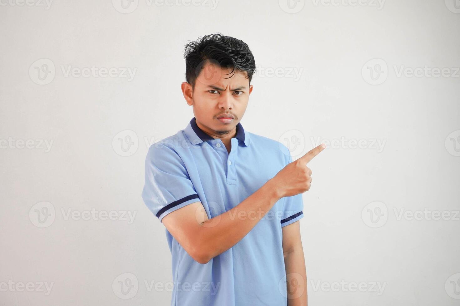 portrait de une réfléchi Jeune asiatique homme avec les doigts montrer du doigt de côté portant bleu t chemise isolé sur blanc Contexte photo