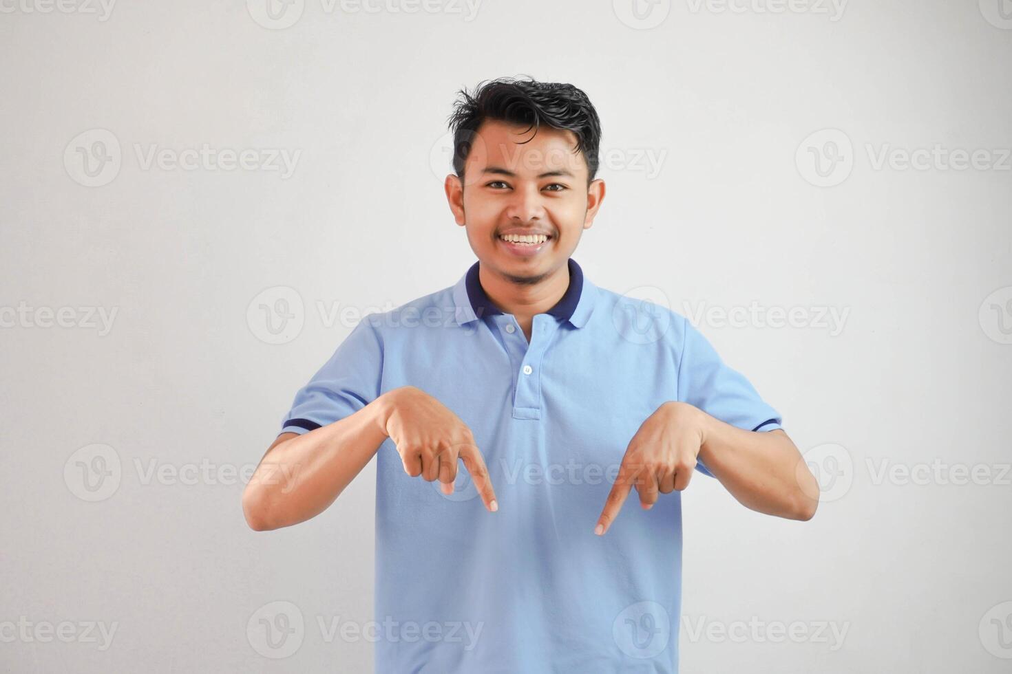 excité Jeune asiatique homme à la recherche caméra doigt montrer du doigt vers le bas portant bleu t chemise isolé sur blanc Contexte photo