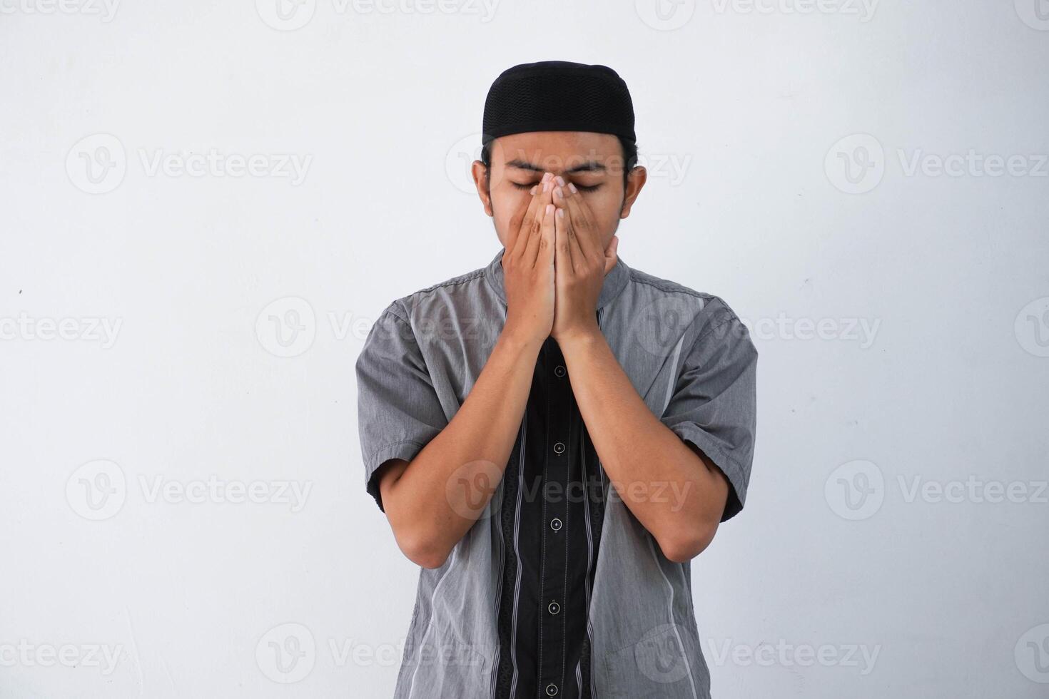 Jeune asiatique musulman homme couverture visage avec mains prier concept, portant gris koko vêtements isolé sur blanc Contexte photo
