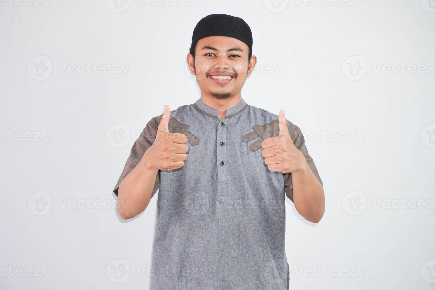 souriant ou content Jeune musulman homme montrant main les pouces en haut portant gris musulman vêtements isolé sur blanc Contexte photo