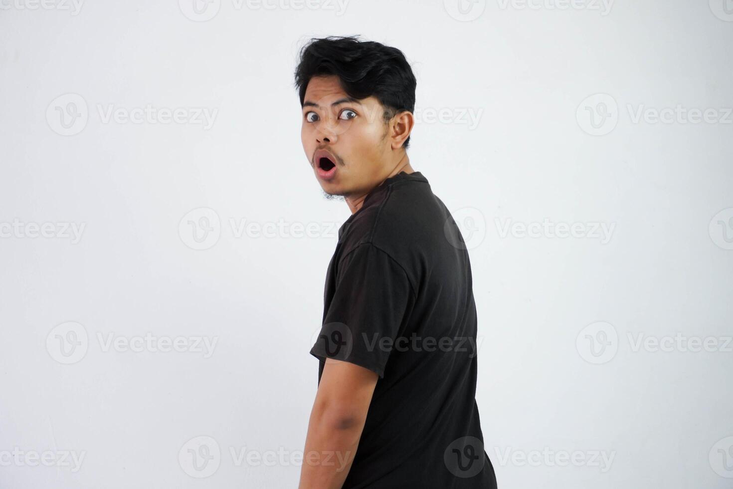 sous le choc asiatique Jeune homme noir t chemise ouvert bouche se sent étonné tour retour à à la recherche caméra isolé sur blanc Contexte photo