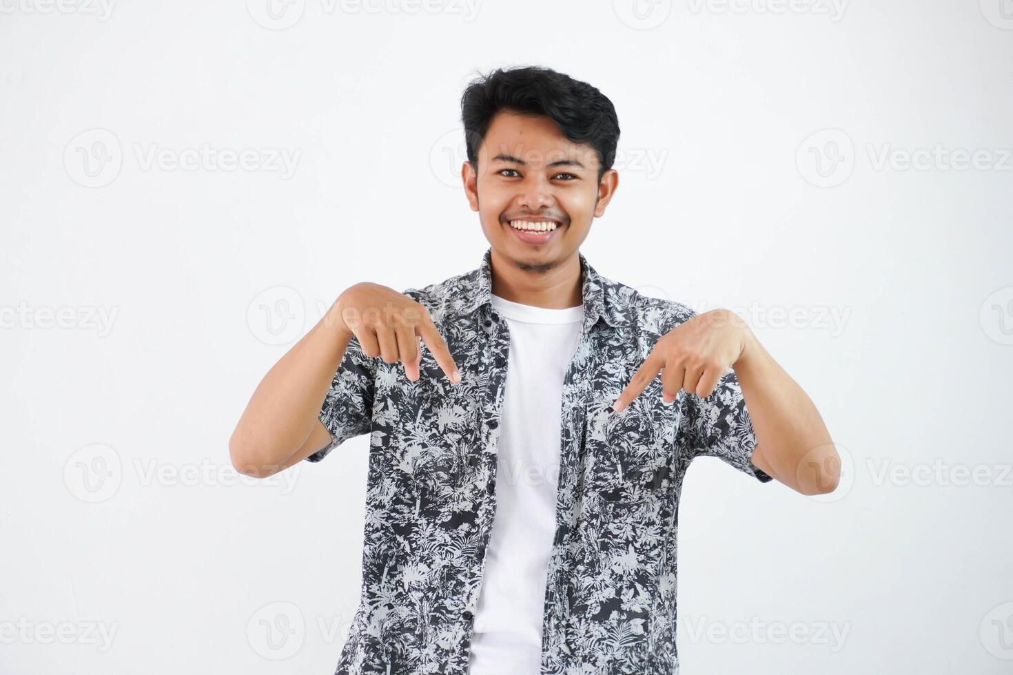 étonné indonésien de bonne humeur Jeune asiatique homme dans noir chemise regards à le caméra et points les doigts vers le bas à espace pour votre présentation, des stands sur isolé blanc arrière-plan, souriant photo