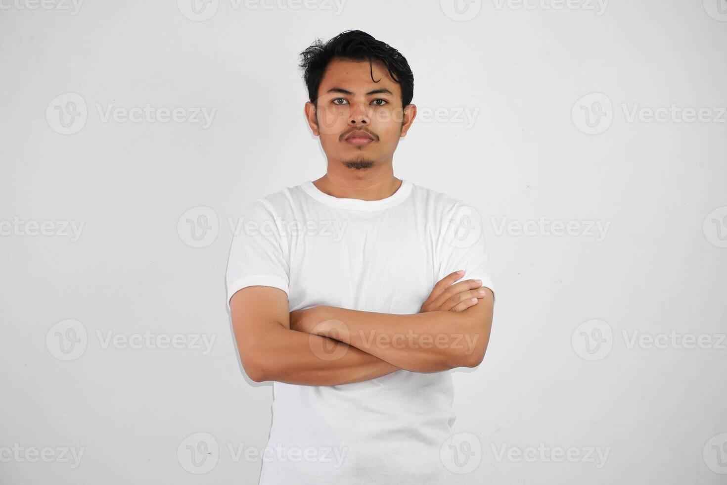 sérieusement asiatique homme franchi bras et à la recherche caméra portant blanc t chemise isolé sur blanc Contexte photo
