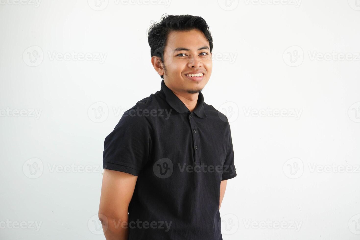 Jeune asiatique homme portant noir polo t chemise content, souriant et de bonne humeur à la recherche à caméra isolé sur blanc Contexte photo