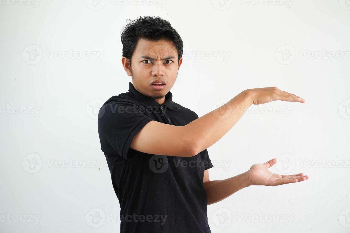 Jeune asiatique homme posant sur une blanc toile de fond sous le choc et étonné en portant une copie espace entre mains, portant noir polo t chemise. photo