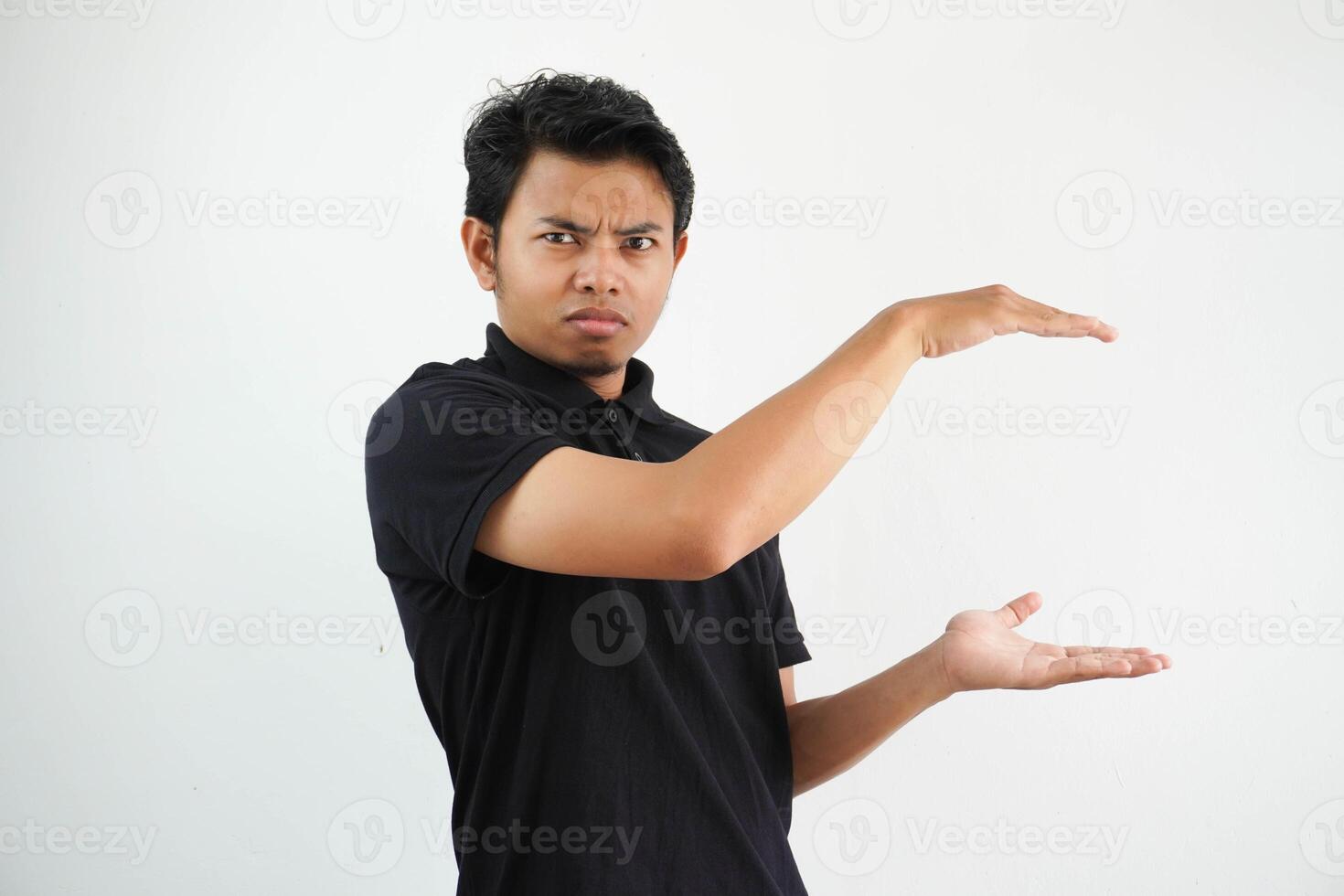 Jeune asiatique homme posant sur une blanc toile de fond sous le choc et étonné en portant une copie espace entre mains, portant noir polo t chemise. photo