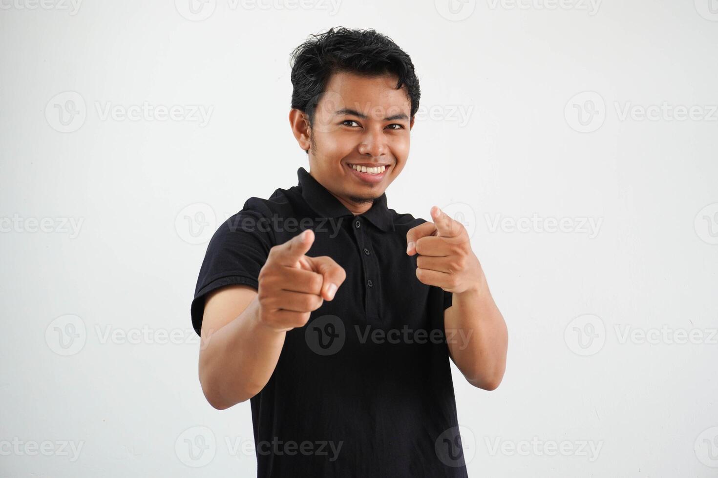 Jeune asiatique homme souriant et montrer du doigt vers caméra portant noir polo t chemise isolé sur blanc Contexte. photo