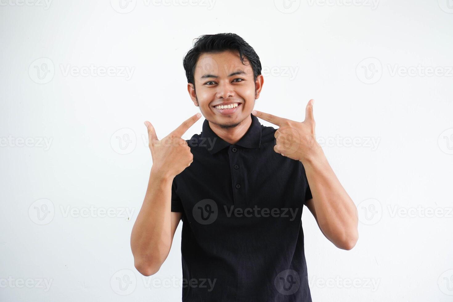 souriant Jeune asiatique homme montrer du doigt à le sien bouche avec content expression portant noir polo t chemise isolé sur blanc Contexte photo