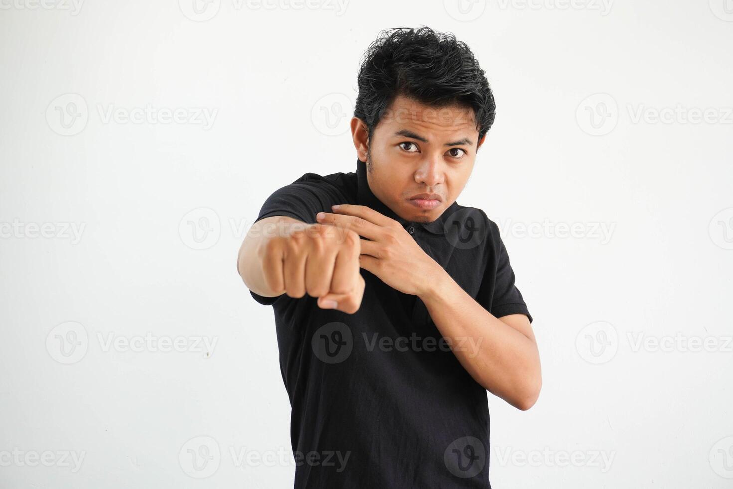 Jeune asiatique homme contre une blanc studio arrière-plan, lancement une coup de poing, colère, combat dû à un argument, boxe, portant noir polo t chemise. photo