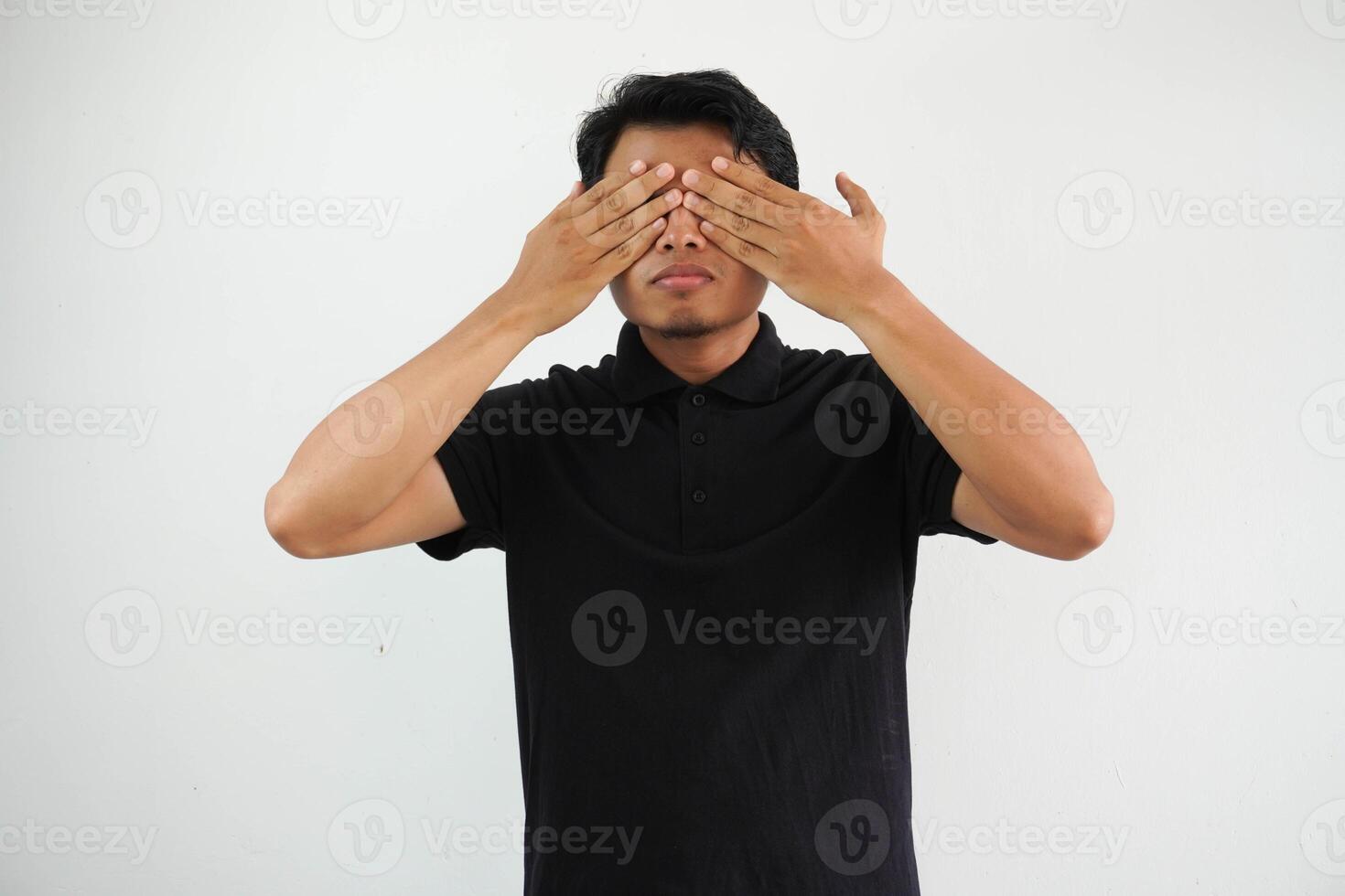 Jeune asiatique homme posant sur une blanc toile de fond peur couvrant yeux avec mains, portant noir polo t chemise. photo