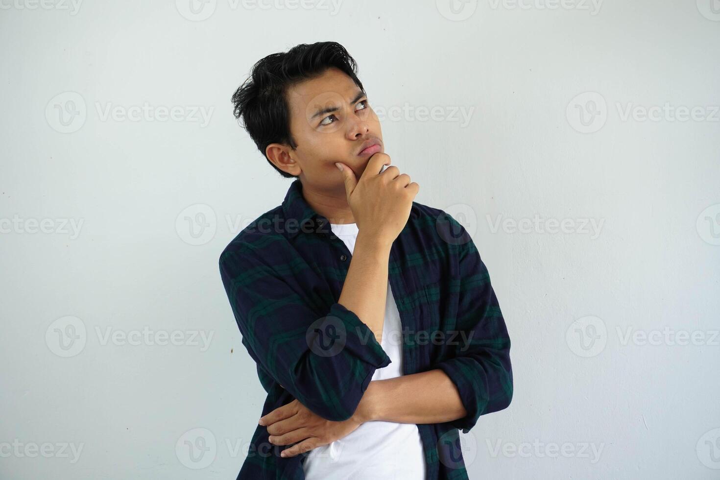 Jeune asiatique homme montrant en pensant pose avec main émouvant le menton tandis que le sien yeux à la recherche à le en haut isolé sur blanc Contexte. photo