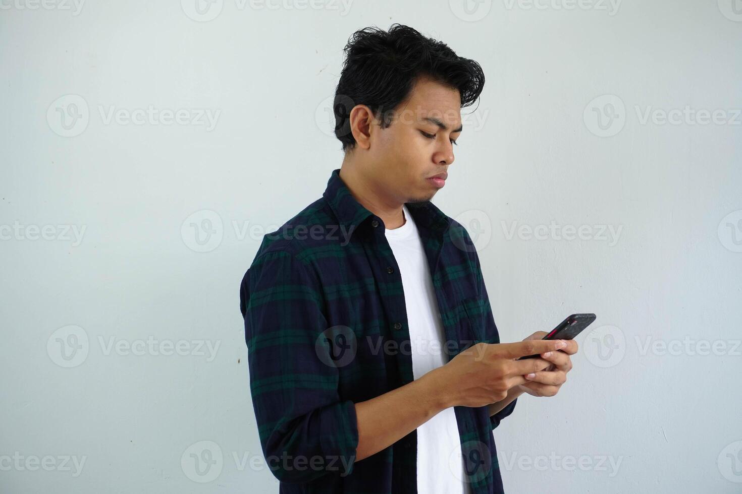 Jeune asiatique homme montrant triste expression tandis que en utilisant à la recherche cette mobile téléphone isolé sur blanc Contexte photo