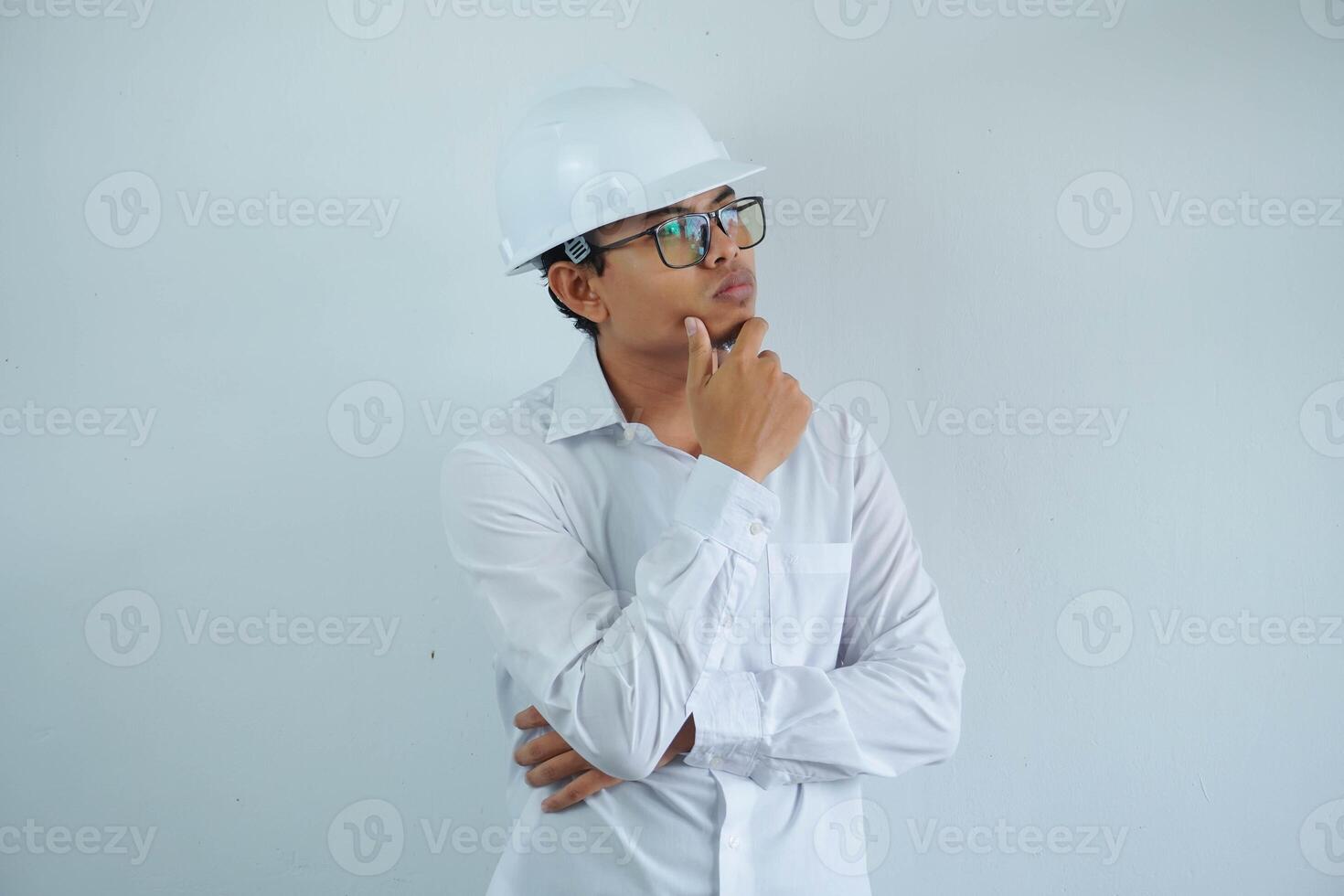 Jeune asiatique Masculin ingénieur portant blanc difficile chapeau en portant menton en pensant pour construction travail isolé sur blanc arrière-plan, copie espace. photo