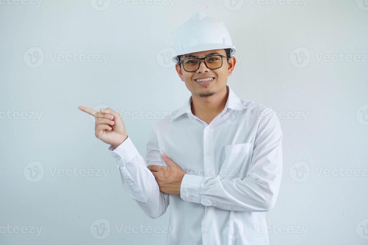 Jeune asiatique architecte homme portant blanc difficile chapeau sécurité casque à la recherche caméra avec doigt montrer du doigt le droite côté isolé sur blanc Contexte photo