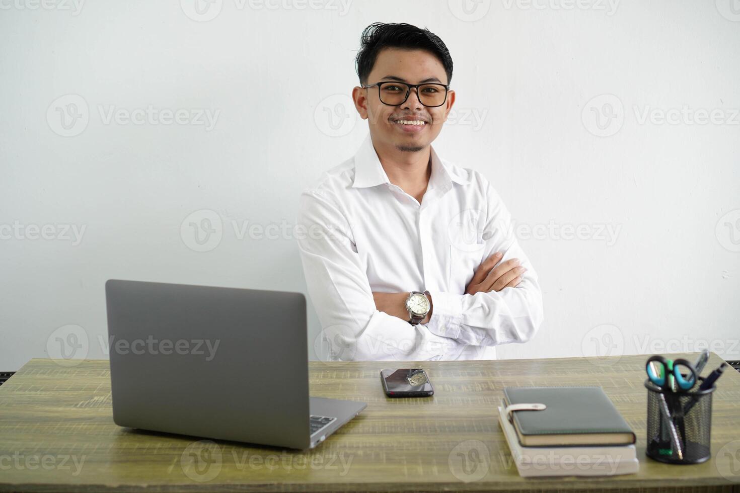 Jeune asiatique homme d'affaire dans une lieu de travail avec bras franchi et à la recherche vers l'avant portant blanc chemise isolé sur blanc Contexte photo