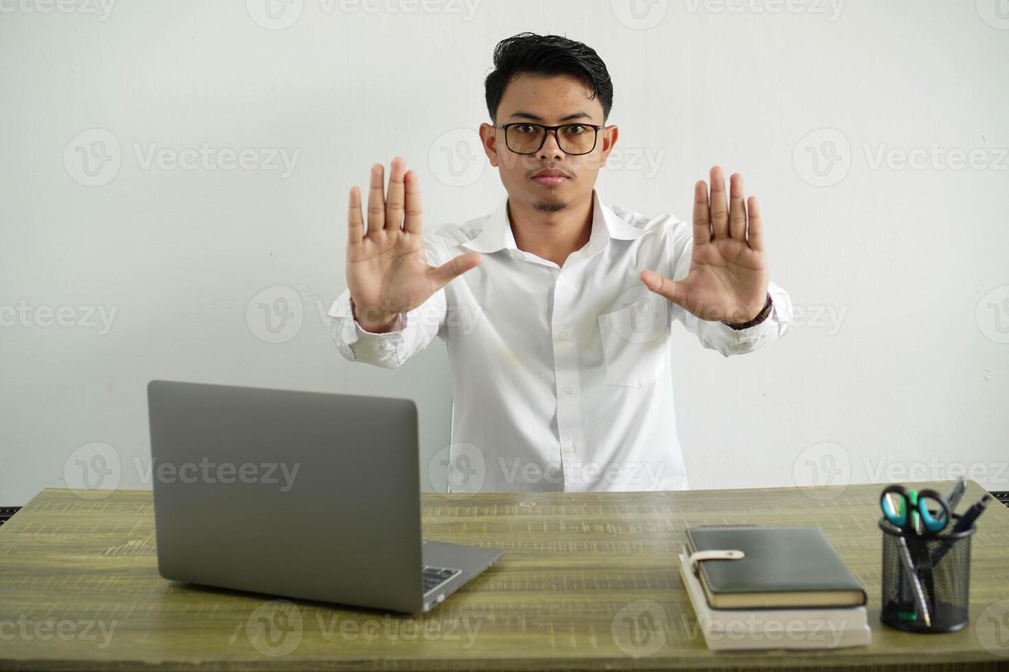 Jeune asiatique homme d'affaire dans une lieu de travail fabrication Arrêtez geste et déçu, portant blanc chemise avec des lunettes isolé photo