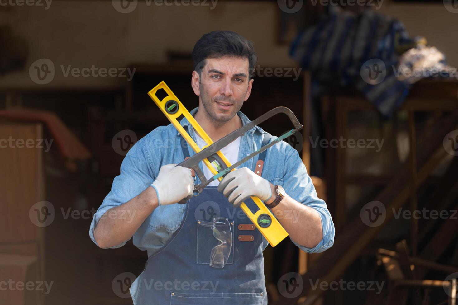 portrait de une Charpentier en portant une esprit niveau et scie à main dans le sien atelier. photo